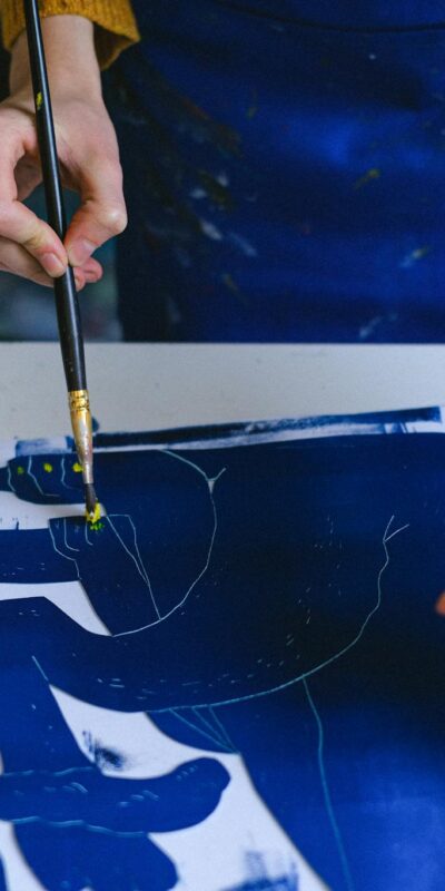 Artist working on blue gouache painting in an indoor studio, focusing on creativity and craft.
